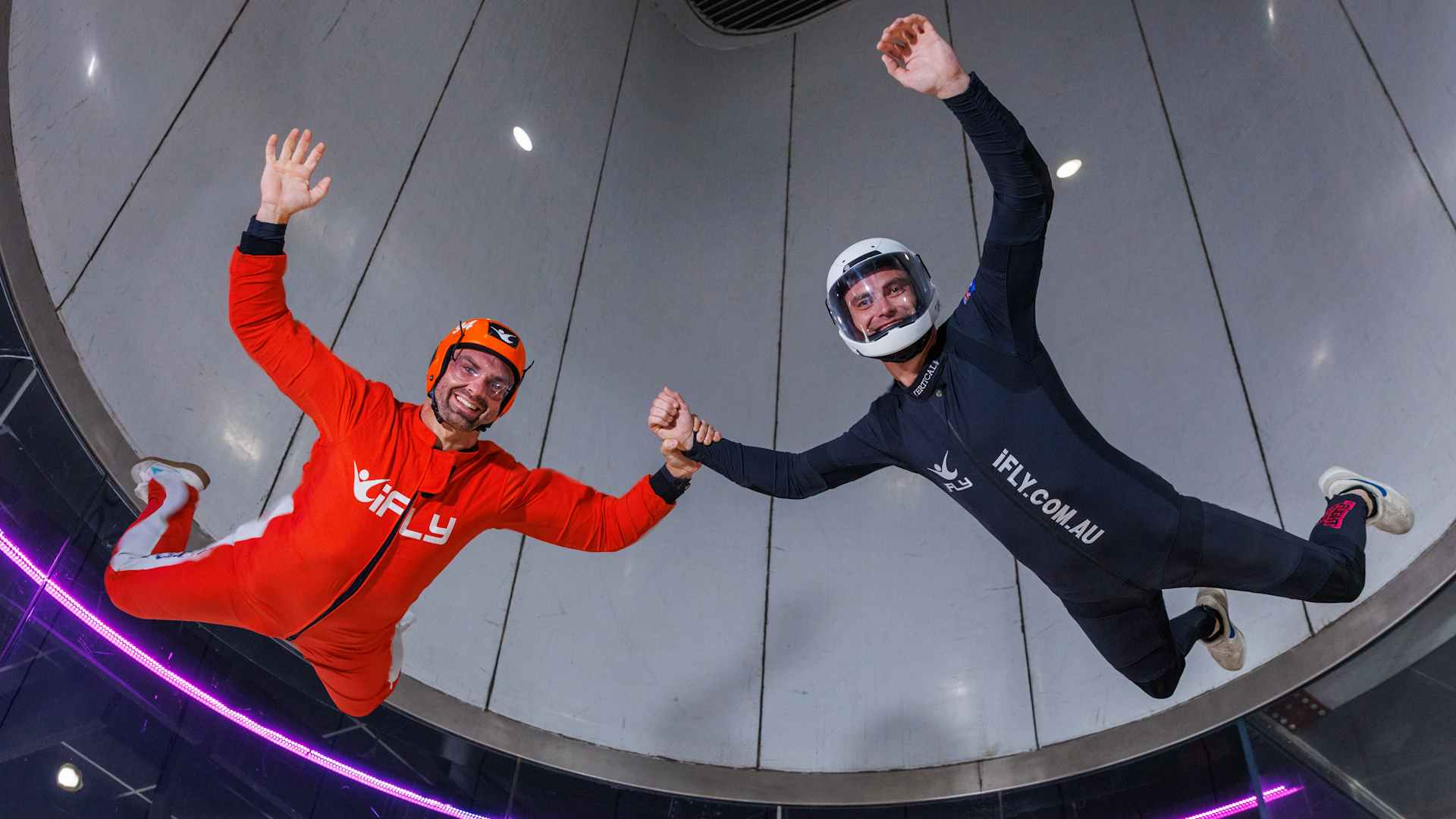 Man performing high fly in orange jumpsuit with instructor in black jumpsuit